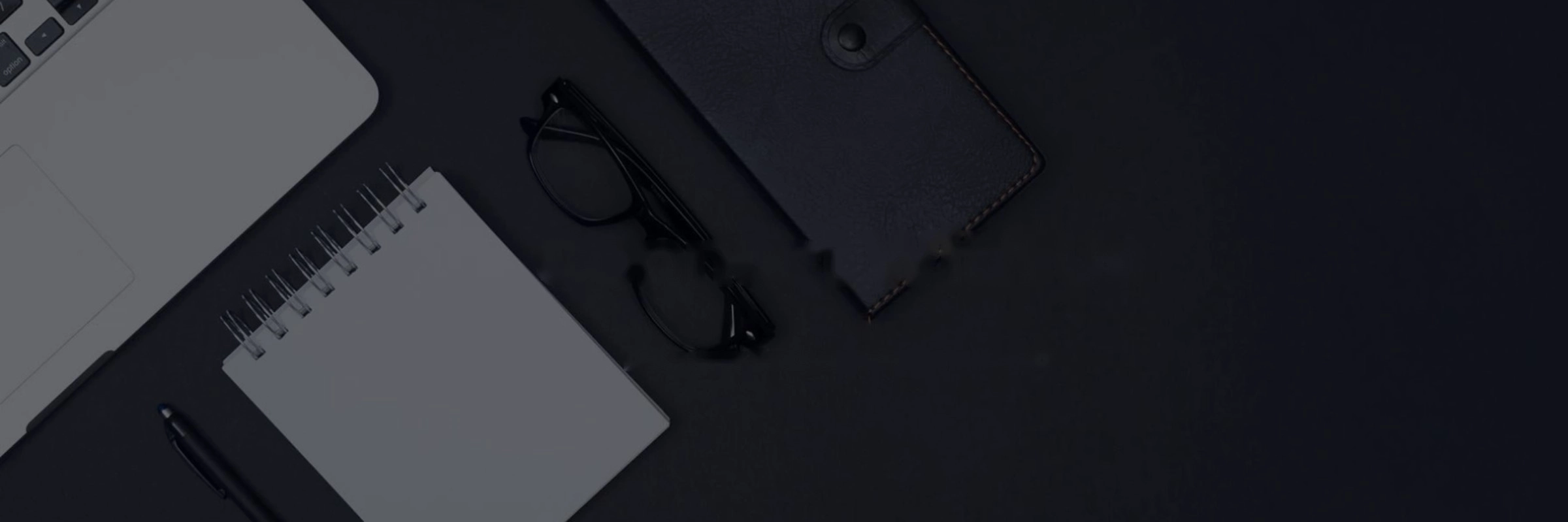 Modern dark desk workspace with a laptop, notebook, glasses and leather portfolio